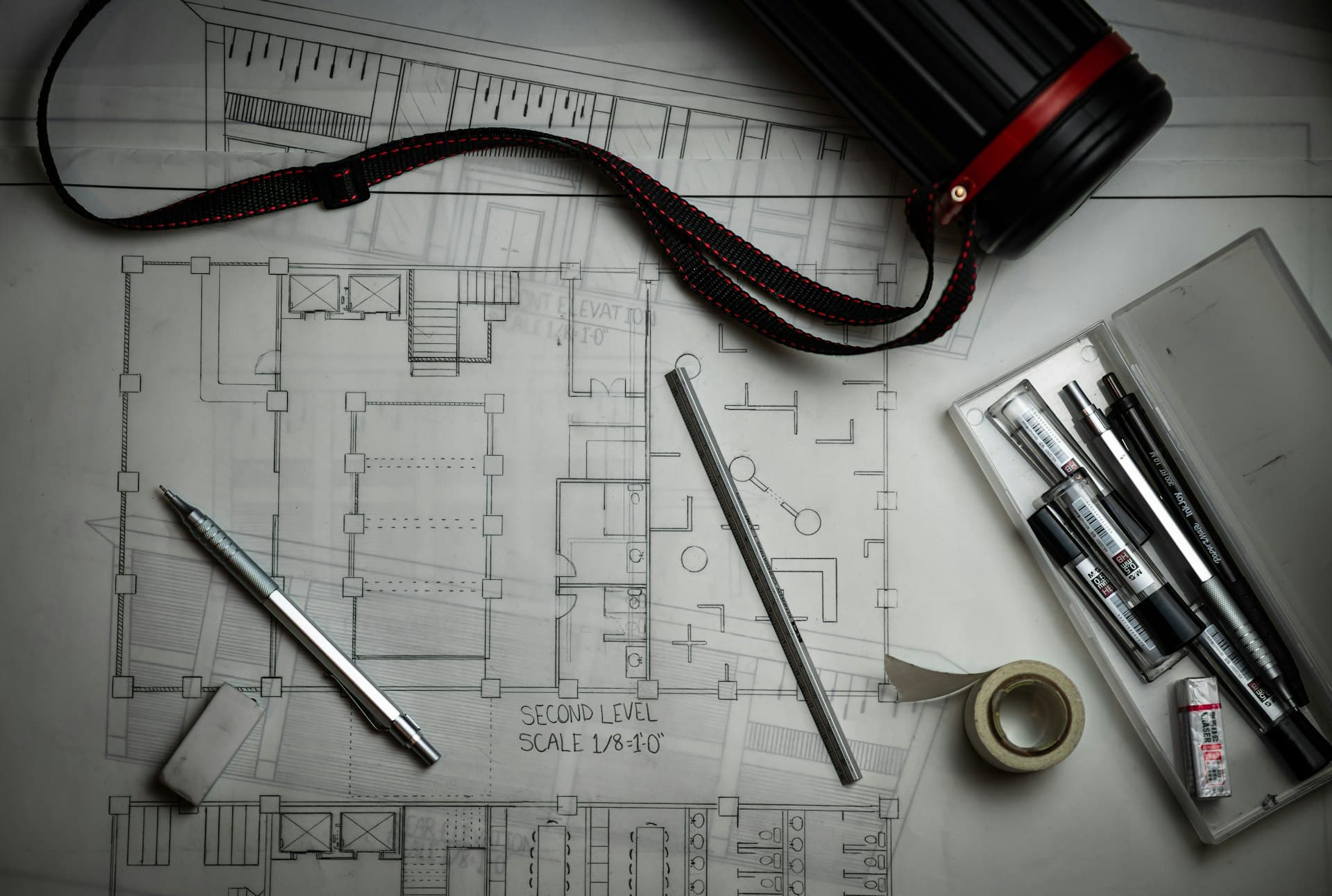 Architectural blueprints laid out with drafting pencils, a metal ruler and a plan tube, ready for a construction quantity takeoff